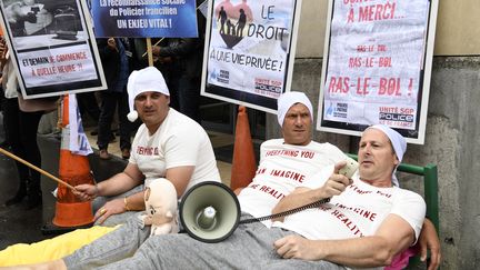 Trois policiers, en pyjama et allongés sur un lit, manifestent le 29 mai 2018 devant un commissariat à Paris.&nbsp; (BERTRAND GUAY / AFP)