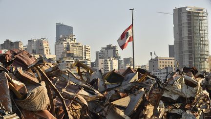 Un drapeau libanais trône, le 3 août 2021, au dessus du port dévasté de Beyrouth où un an plus tôt,&nbsp;des centaines de tonnes de nitrate d'ammonium, stockées depuis des années dans un entrepôt délabré, ont explosé. (HUSSAM SHBARO / ANADOLU AGENCY / AFP)