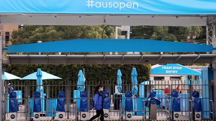 Une femme masquée marche devant l'entrée principale de l'Open d'Australie de tennis, à Melbourne, le 4 février 2021. (DAVID GRAY / AFP)