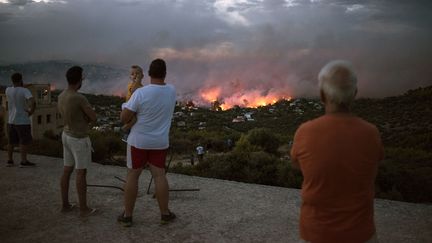 Des Grecs regardent l'incendie qui ravage Rafina, dans l'Attique (Grèce), la région d'Athènes, le 23 juillet 2018. (ANGELOS TZORTZINIS / AFP)