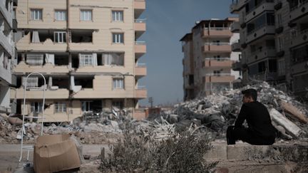 Un homme contemple les débris d'un immeuble effondré dans lequel a péri un de ses cousins, le 28 février 2023, à Nurdagi (Turquie). (HIROTO SEKIGUCHI / YOMIURI / AFP)