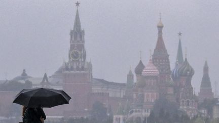 Un passant avec un parapluie, devant le Kremlin, à Moscou, le 14 septembre 2022. (YURI KADOBNOV / AFP)