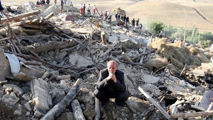 Dimanche, les habitants de Varzaqan ne peuvent que constater l'&eacute;tendue des d&eacute;g&acirc;ts. De nombreuses maisons construites en briques ou en terre ont &eacute;t&eacute; balay&eacute;es. L'homme est assis sur les d&eacute;combres de sa maison. (ATTA KENARE / AFP)