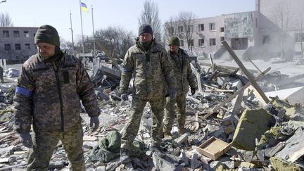 Des soldats ukrainiens cherchent des corps dans les débris de l'école militaire touchée par des roquettes russes la veille, à Mykolaiv, dans le sud de l'Ukraine, le 19 mars 2022. (BULENT KILIC / AFP)