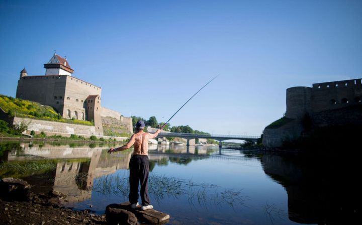 Un homme pêche sur la Narva, côté estonien, en juin 2016. Le château d'Hermann, à gauche, fait face à la forteresse d'Ivangorod, situé sur la rive russe du fleuve. (KAY NIETFELD / DPA)