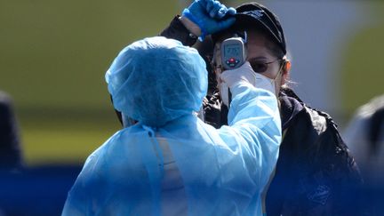 Une personne mesure la température corporelle d'un passager débarquant du navire de croisière "Diamond Princess", à Yokohama (Japon) le 21 février 2020. (PHILIP FONG / AFP)