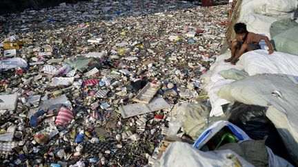 Un enfant au dessus d'une rivière pleine de déchets en plastique à Manille (Philippines). (NOEL CELIS / AFP)