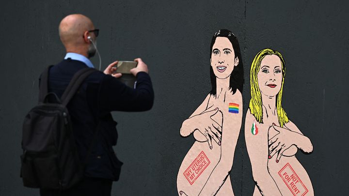 L'artiste aleXsandro Palombo illustre le débat sur la GPA, le 22 mai 2023, à Milan (Italie), avec une fresque montrant la cheffe du Parti démocrate, Elly Schlein, et la Première ministre, Giorgia Meloni. (GABRIEL BOUYS / AFP)