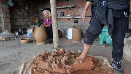 Elle travaille un mélange d'argile et de briques concassées foulé par sa belle-sœur : les briques - l'une des rares touches de modernité dans le procédé - remplacent les débris de pots cassés qu'on ajoutait autrefois pour solidifier l'argile cru. (FETHI BELAID / AFP)