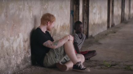 Le&nbsp;chanteur Ed Sheeran avec un enfant du Liberia, dans une vidéo pour la campagne Red Nose Day de l'ONG Comic Relief. (REDNOSEDAY.ORG / YOUTUBE)