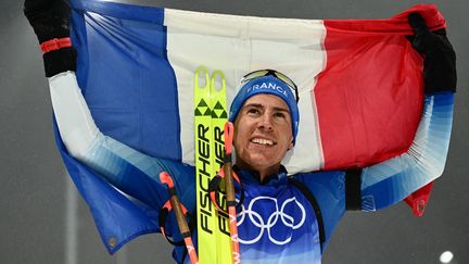 Quentin Fillon Maillet pose avec le drapeau tricolore après sa victoire sur la poursuite des Jeux olympiques, le 13 février 2022. (JEWEL SAMAD / AFP)