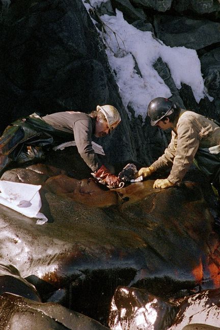 Des nettoyeurs frottent un rocher couvert de pétrole, sur Naked Island, dans la baie du Prince-William, le 2 avril 1989. (CHRIS WILKINS / AFP)