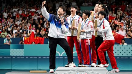 Le pongiste sud-coréen Lim Jonghoon (à gauche) célèbre sa médaille de bronze avec les nord-coréens Ri Jong Sik et Kim Kum Yong, les athlètes chinois Wang Chuqin et Sun Yingsha, ainsi qu'avec sa compatriote Shin Yubin à l'issue de l'épreuve du double mixte aux Jeux olympiques de Paris 2024, le 30 juillet 2024. (JUNG YEON-JE / AFP)