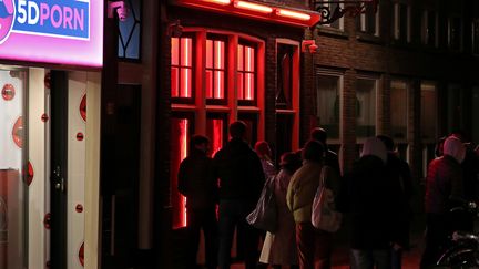 Des personnes devant la vitrine d'une maison close, le 3 avil 2019, à Amsterdam.&nbsp; (YVES HERMAN / REUTERS)