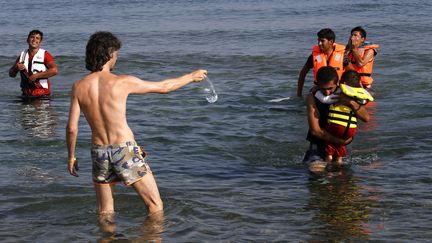 Sur les c&ocirc;tes grecques,&nbsp;touristes et migrants se m&eacute;langent. Un europ&eacute;en offre de l'eau &agrave; des iraniens qui arrivent sur l'ile de Kos&nbsp;en Gr&egrave;ce depuis la c&ocirc;te turque sur un canot le 15 ao&ucirc;t 2015. Environ 124 000 personnes auraient atteint les c&ocirc;tes grecques cette ann&eacute;e par la mer. (YANNIS BEHRAKIS / REUTERS)