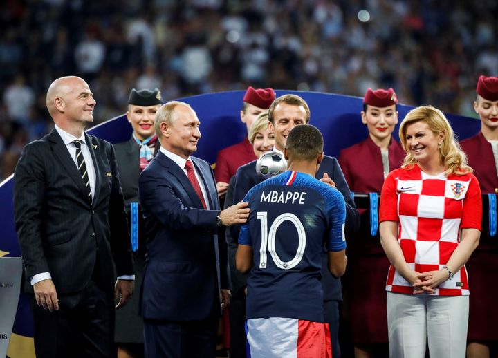 Le président français Emmanuel Macron, l'ancienne présidente croate Kolinda Grabar Kitarovic (à d.), le président russe Vladimir Poutine et le président de la FIFA Gianni Infantino (à g.) saluent le français Kylian Mbappé lors de la cérémonie de remise des prix lors de la finale de la Coupe du monde 2018, après la victoire de la France face à la Croatie, à Moscou, le 15 juillet 2018. 
 (SEBNEM COSKUN / ANADOLU AGENCY)