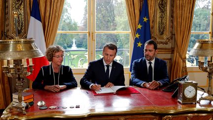 Le président de la République, Emmanuel Macron, aux côtés de Muriel Pénicaud, la ministre du Travail, et de Christophe Castaner, porte-parole du gouvernement, lors de la signature des ordonnances réformant le droit du travail, vendredi 22 septembre à l'Elysée. (PHILIPPE WOJAZER / POOL)