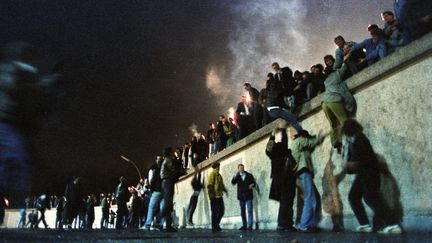 Des citoyens est-allemands grimpent sur le mur&nbsp;de Berlin (ex-RDA), le 9 novembre 1989. (STRINGER  / REUTERS)