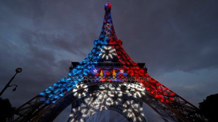 Alors que la nuit tombe, la tour Eiffel s'illumine aux couleurs de la France, et arbore fièrement deux étoiles, symboles des deux victoires, en vingt ans, de la France en Coupe du monde de football.&nbsp; (PHILIPPE WOJAZER / REUTERS)