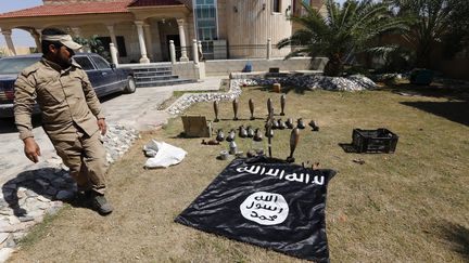 Un homme ayant rejoint une milice chiite passe devant un drapeau et des munitions de l'Etat islamique, dans la province de&nbsp;Salahuddin (Irak), le 15 mars 2015. (THAIER AL-SUDANI / REUTERS)