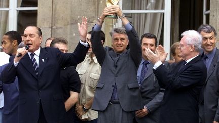 Le président de la République Jacques Chirac (g.), l'entraîneur de l'équipe de France de football (centre) et le Premier ministre Lionel Jospin (d.) avec le trophée de la Coupe du monde 1998 à l'Élysée, à l'issue du défilé du 14 juillet. (GABRIEL BOUYS / AFP)