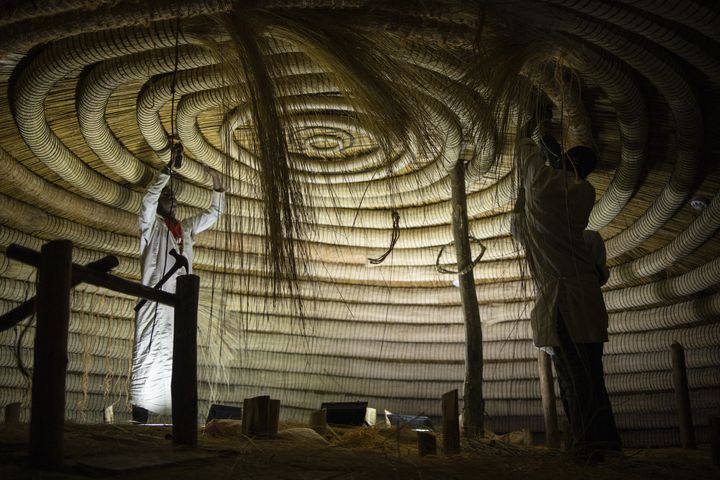 Des artisans fixent les anneaux circulaires au plafond de l'un des bâtiments appartenant aux tombeaux royaux de Kasubi à Kampala, en Ouganda, le 13 juin 2023. (STUART TIBAWESWA / AFP)