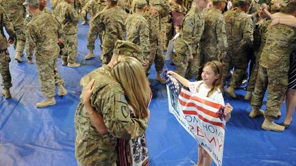 Un soldat de retour d'Afghanistan enlace son &eacute;pouse tandis que sa fille d&eacute;ploie une banderole de bienvenue &agrave; Fort Stewart (Georgie), le 12 mars 2012. (ERIK S. LESSER / EPA / MAXPPP)