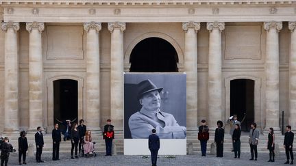Le président français Emmanuel Macron se tient devant un portrait géant du défunt acteur français Michel Bouquet lors d'un hommage national à l'hôtel des Invalides à Paris le 27 avril 2022. (LUDOVIC MARIN / AFP)