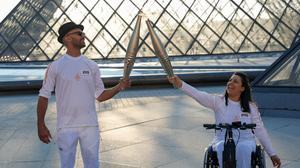 L'artiste JR et l'athlète Sandra Laoura se relaient sur le parcours de la flamme olympique au musée du Louvre, le 14 juillet 2024. ((GEOFFROY VAN DER HASSELT / AFP))