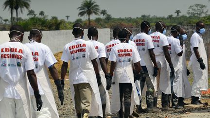 Des travailleurs &eacute;quip&eacute;s de masques marchent en ligne au cr&eacute;matorium de Monrovia (Liberia), le 7 mars 2015, o&ugrave; sont re&ccedil;ues les d&eacute;pouilles des victimes du virus Ebola. (ZOOM DOSSO / AFP)