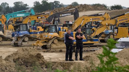 Des policiers montent la garde, le 7 juin 2024, devant les engins de construction sur le site de l'A69 où une manifestation est attendue (ED JONES / AFP)