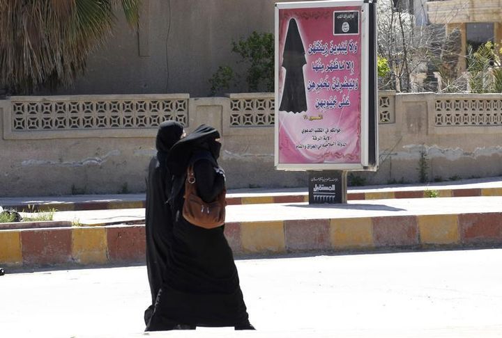 A Raqqa (Syrie),&nbsp;le 31 mars 2014,&nbsp;des femmes int&eacute;gralement voil&eacute;es passent devant un panneau publicitaire sur lequel est affich&eacute; la loi de l'Etat islamique. (REUTERS)