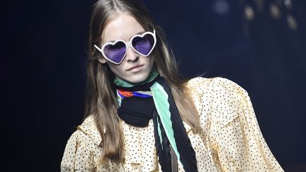 Gucci a délivré une ode aux années 80, avec un show foisonnant de costumes droits, franges et paillettes. Le styliste Alessandro Michele a opté pour un style chic. Dans une quasi-obscurité, percée de quelques flashs de lumière, il a présenté une collection riche en lunettes rondes, satin et broderies colorées et scintillantes. "Nous vivons dans une société où nous sommes obsédés par la vérification et moi je veux vous hypnotiser", a-t-il expliqué. D'où un podium évoquant l'Atlantide une nuit de brouillard, hérissé de sculptures massives des plus grands symboles de l'humanité comme un Bouddha souriant et Toth, le plus sage des dieux égyptiens. Les vêtements embrassaient le passé, à l'exemple d'un costume de satin aux étoiles de paillettes semblant sorti de la garde-robe de David Bowie. Un costume trois-pièces marron rappelait une vieille photo Kodachrome, abstraction faite des énormes bagues incrustées et des larges lunettes de soleil blanches qui l'accompagnent. Les garçons défilent en short, cravate, gilet à l'effigie de Bugs Bunny ou pantalon de dentelle tandis que les filles portent des robes de tulle ou des vestes Prince de Galles.
 (Miguel MEDINA / AFP)