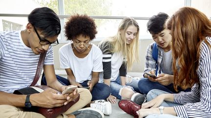 Des étudiants assis ensemble qui utilisent leur smartphone. (illustration) (DINOCO GRECO / MAXPPP)