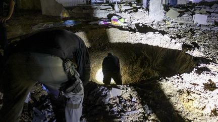 Des membres des forces de l'ordre israéliennes inspectent un cratère laissé par un missile près d'un bâtiment scolaire à Gedera, dans le sud d'Israël, le 1er octobre 2024. (MENAHEM KAHANA / AFP)