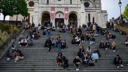 Des gens assis sur les escaliers devant la Basilique du Sacré Coeur à Paris dans le 18e arrondissement, le 12 mai 2020. (BERTRAND GUAY / AFP)