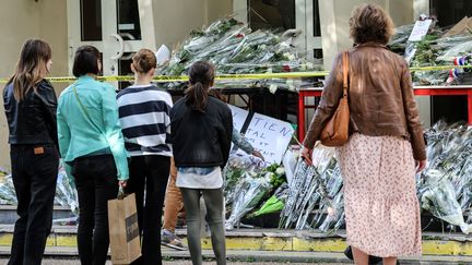 Des personnes devant des fleurs déposées en hommage au professeur Dominique Bernard, le 14 octobre 2023 à Arras (Pas-de-Calais). (DENIS CHARLET / AFP)