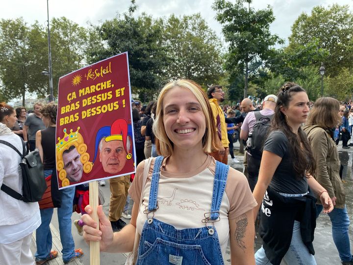 Julie, 34, demonstrates with a humorous placard under her arm, in Paris, on September 7, 2024. (ELOISE BARTOLI / FRANCEINFO)