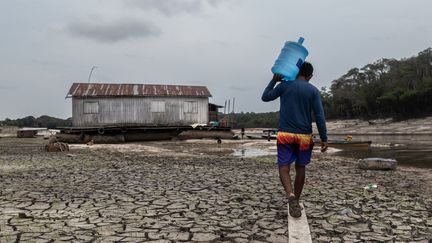 Un homme transporte un bidon d'eau potable dans une maison flottante, alors que le fleuve est à sec, près de Manaus, au Brésil, le 16 octobre 2023. (RAPHAEL ALVES / MAXPPP)