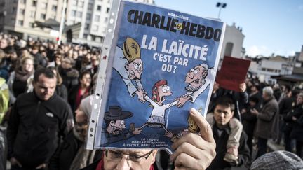 Un manifestant de la marche républicaine du 11 janvier 2015 brandit une Une de Charlie Hebdo sur la laïcité.&nbsp; (JEAN-PHILIPPE KSIAZEK / AFP)