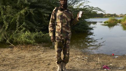 Le 7 novembre 2018, le soldat tchadien Ali Adam Agar pose avec un smartphone devant le lac Tchad. Ali utilise son smartphone pour écouter les versets du Coran pendant qu'il patrouille au bord du lac.  (MICHELE CATTANI / AFP)