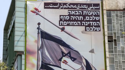 Une banderole représentant des missiles et des drones survolant un drapeau israélien déchiré est accrochée sur la façade d’un bâtiment.  sur la place de la Palestine à Téhéran, le 14 avril 2024. Elle porte un avertissement : 