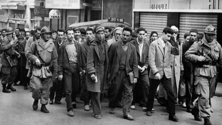 Des soldats français escortent des manifestants algériens vers un point de contrôle de leur identité, le 11 décembre 1960, à Alger.&nbsp; (JEAN-CLAUDE COMBRISSON / AFP)