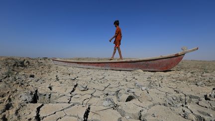 Sécheresse en Irak : un garçon marche sur une embarcation abandonnée sur le lit asséché&nbsp;d'une section des marais du sud du pays en recul à Chibayish, dans la province de Dhi Qar, le 28 juin 2022. (ASAAD NIAZI / AFP)