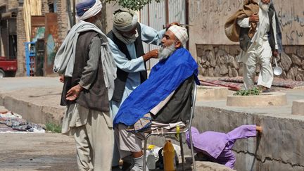 Un homme se fait couper les cheveux par un barbier dans une rue d'Herat (Afghanistan), le 2 juin 2013. (AREF KARIMI / AFP)