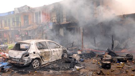 La carcasse d'un v&eacute;hicule devant des commerces incendi&eacute;s, apr&egrave;s une explosion au march&eacute; de Jos (Nigeria), le 20 mai 2014. (AFP)