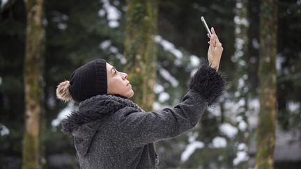 Une femme prend une photo avec son téléphone portable, dans une forêt suisse, le 21 décembre 2017.&nbsp; (BRIGITTE BLÄTTLER / MOMENT RF / GETTY IMAGES)