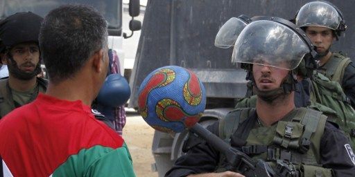 Un jeune Palestinien jongle avec un ballon devant un barrage israélien lors d'une manifestation de soutien aux grévistes palestiniens de la faim, le 11 juin 2014 en Cisjordanie. (ABBAS MOMANI / AFP)