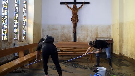 Des volontaires raclent le sol d'une église inondée, à Paiporta. (JOSE JORDAN / AFP)