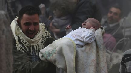 Un homme porte un b&eacute;b&eacute; ayant surv&eacute;cu &agrave; une attaque a&eacute;rienne attribu&eacute;e &agrave; l'arme syrienne pr&egrave;s de Damas (Syrie), le 7 janvier 2014. (BASSAM KHABIEH / REUTERS)